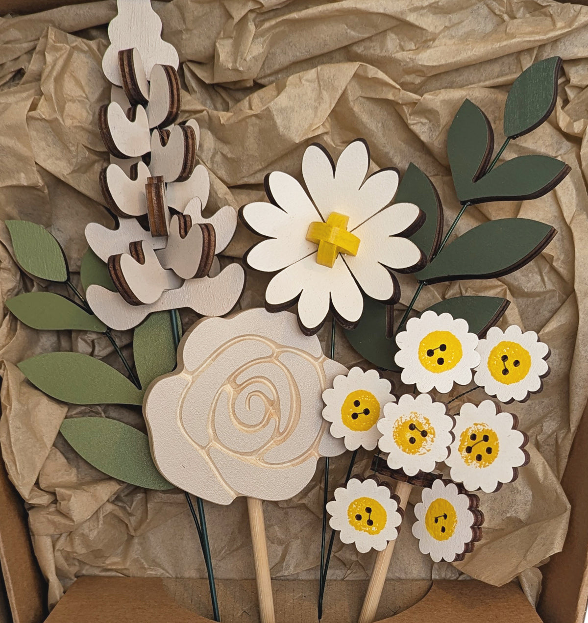 Signature Blooms in Sunny Side, a close crop of all four wooden blooms and two foliage stems in grey and white with a touch of sunshine yellow, arranged in the box against brown tissue