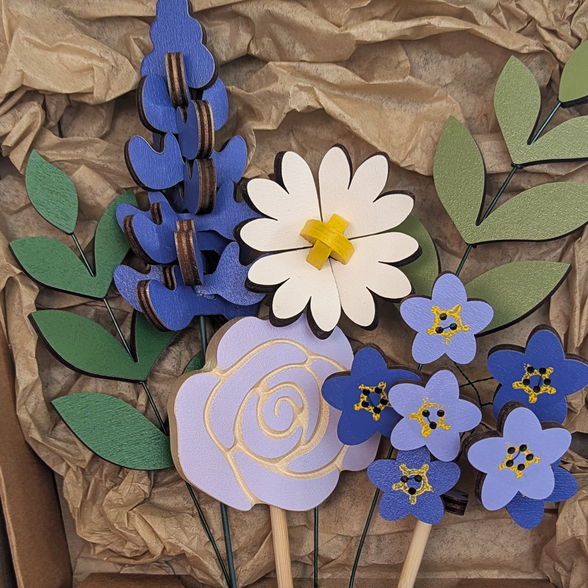 Signature Blooms in Parma Violet, a close crop of all four wooden blooms and two foliage stems in violet and lilac, arranged in the box against brown tissue