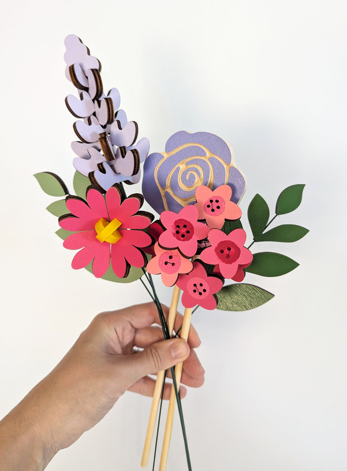 Signature Blooms in Macaron, four wooden blooms and two foliage stems in bright pink and violet, held in one hand