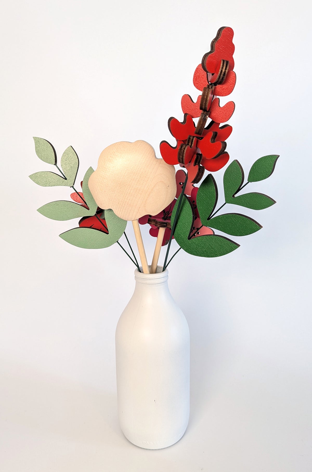 Signature Blooms in Framboise, four wooden blooms and two foliage stems in red, fuchsia and pink, seen from behind