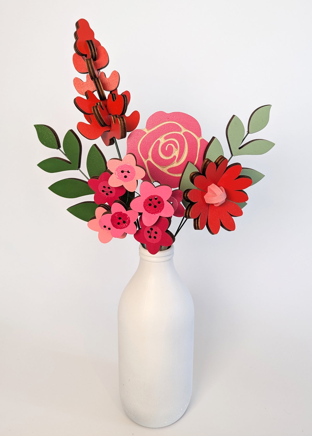 Signature Blooms in Framboise, four wooden blooms and two foliage stems in red, fuchsia and pink, in a vase 