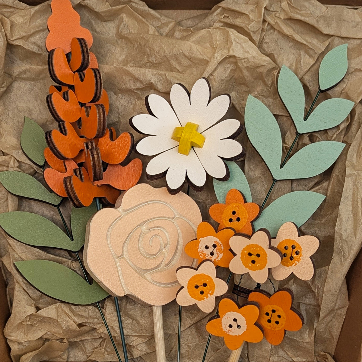 Signature Blooms in Satsuma, a close crop of all four wooden blooms and two foliage stems in warm orange, arranged in the box against brown tissue 