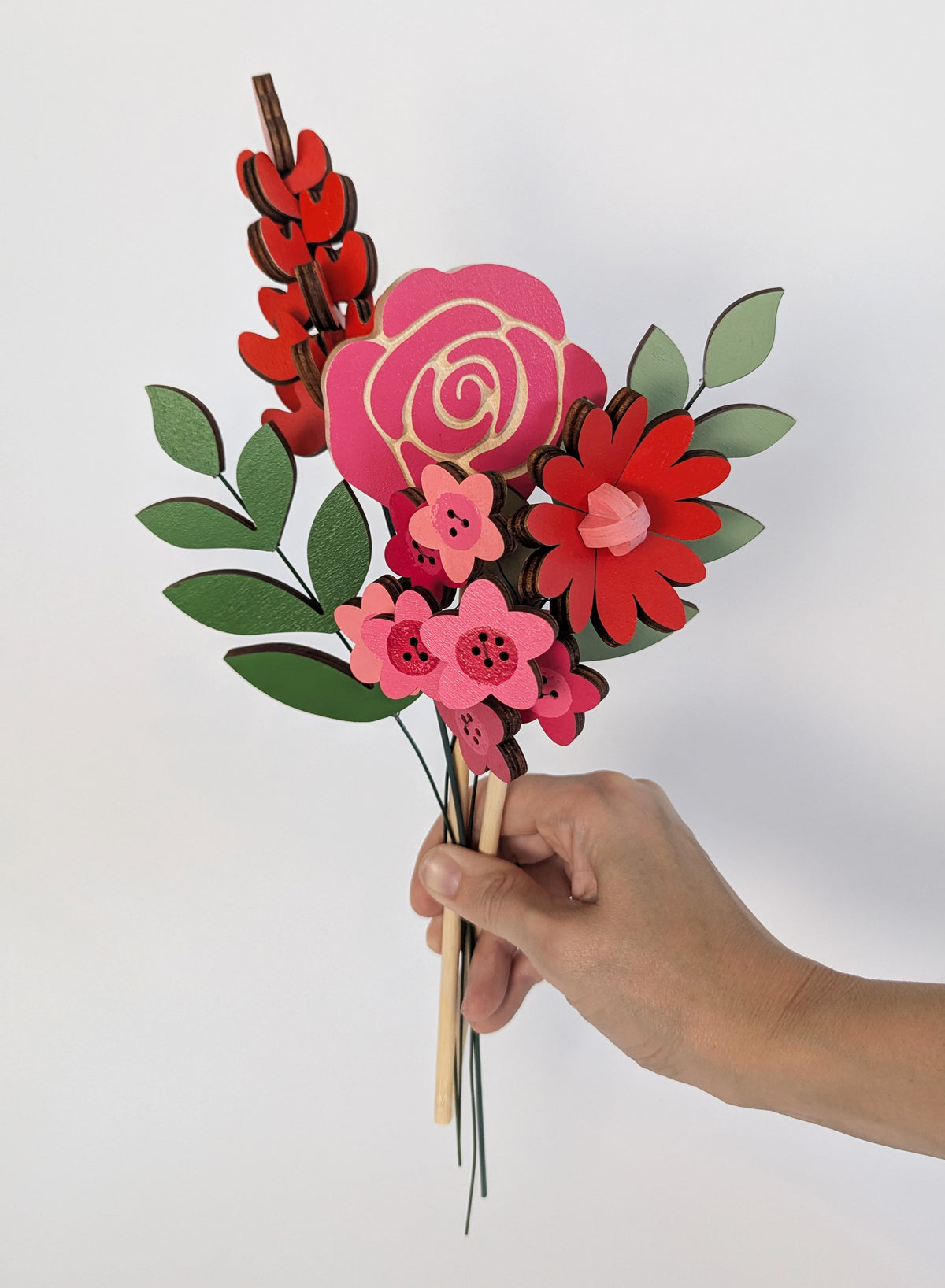 Signature Blooms in Framboise, four wooden blooms and two foliage stems in red, fuchsia and pink, held in one hand 