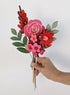 Signature Blooms in Framboise, four wooden blooms and two foliage stems in red, fuchsia and pink, held in one hand 