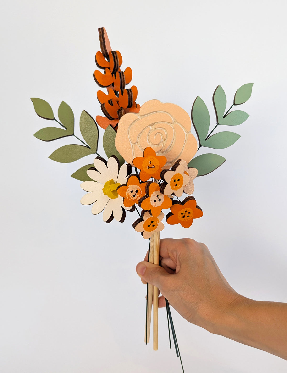 Signature Blooms in Satsuma, four wooden blooms and two foliage stems in warm orange, held in one hand 