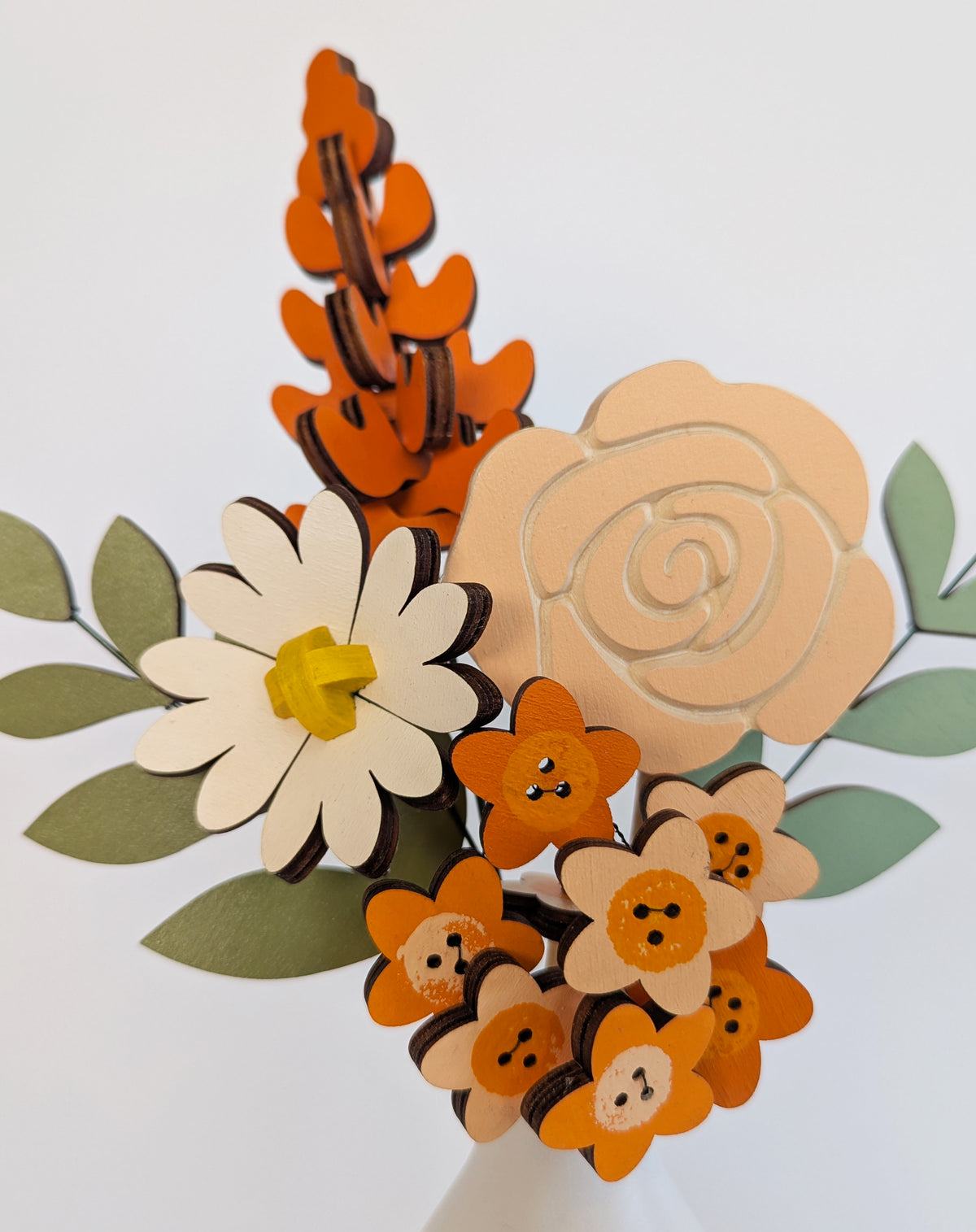 Signature Blooms in Satsuma, four wooden blooms and two foliage stems in warm orange, a macro detail of the painted facets 