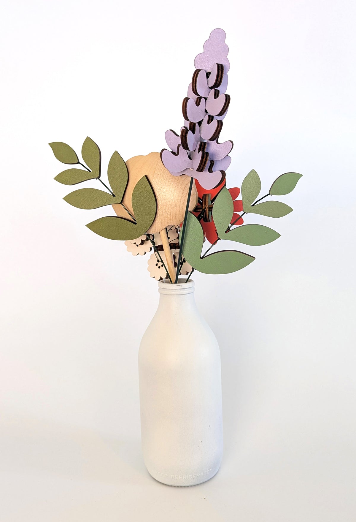 Signature Blooms in Sorbet, four wooden blooms and two foliage stems in muted mustard, lilac, peach, coral and sage, seen from behind 