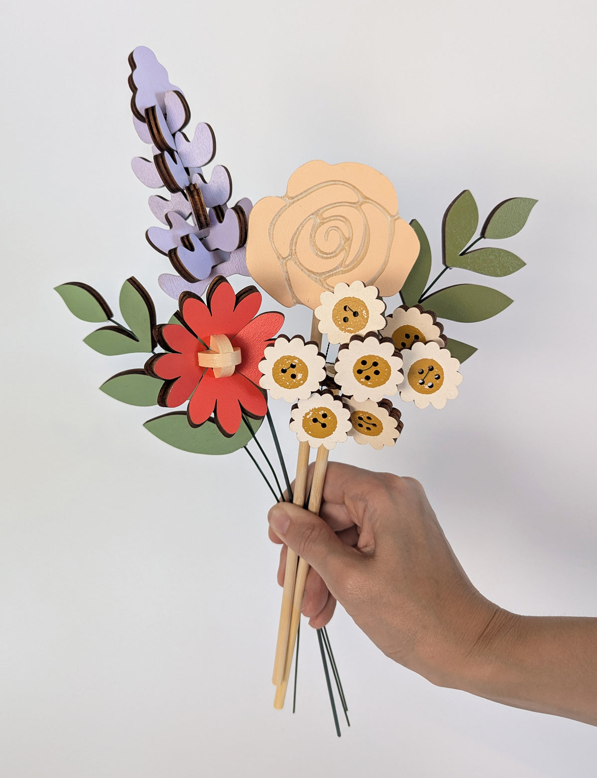 Signature Blooms in Sorbet, four wooden blooms and two foliage stems in muted mustard, lilac, peach, coral and sage, held in one hand 