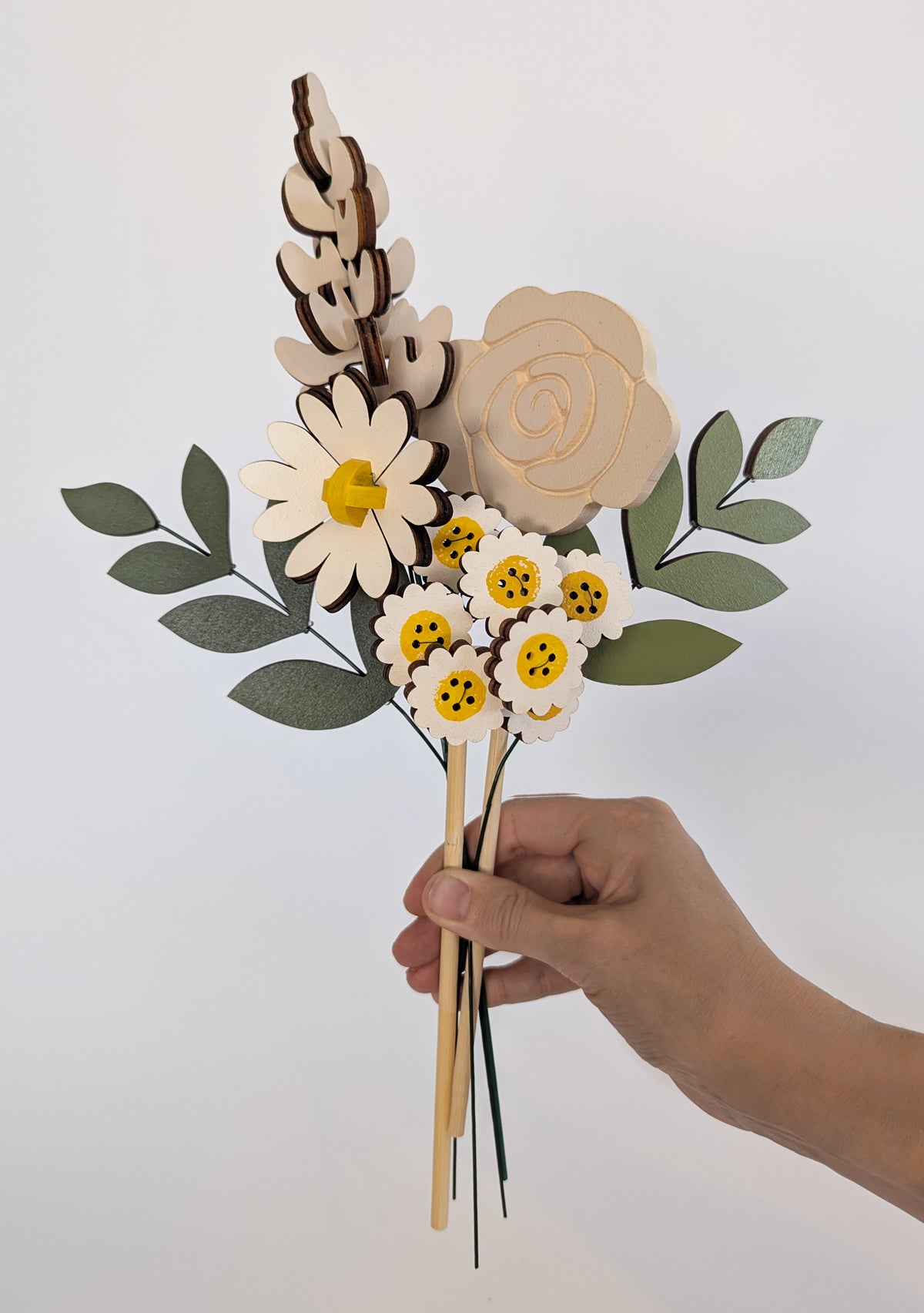 Signature Blooms in Sunny Side, four wooden blooms and two foliage stems in grey and white with a touch of sunshine yellow, held in one hand 